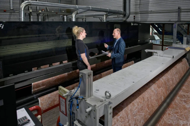 Man en vroue in een fabriekshal. Man voert een RI&E uit en geeft advies